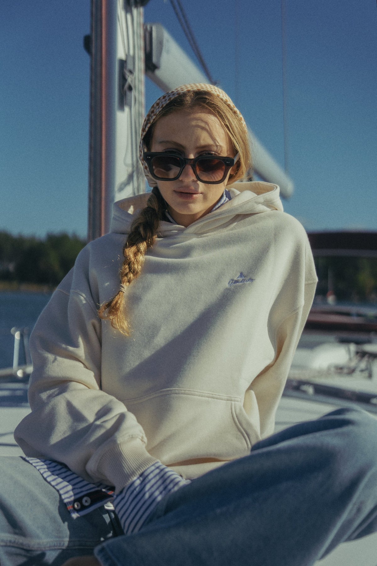 Kvinna i Gårdisto Hoodie i sand sitter på däcket av en segelbåt