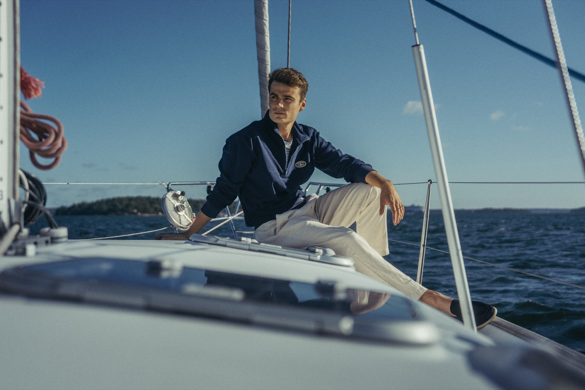 Man seated on the deck of a sailing boat in the Gårdisto Fleece Half-Zip in navy.