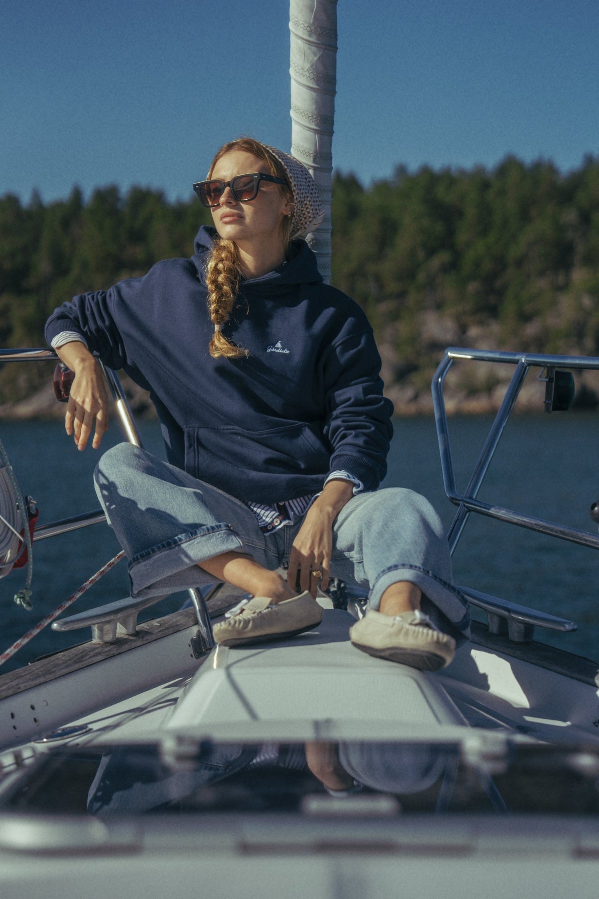 Woman sitting on the deck of a sailing boat in The Gårdisto Hoodie in navy.