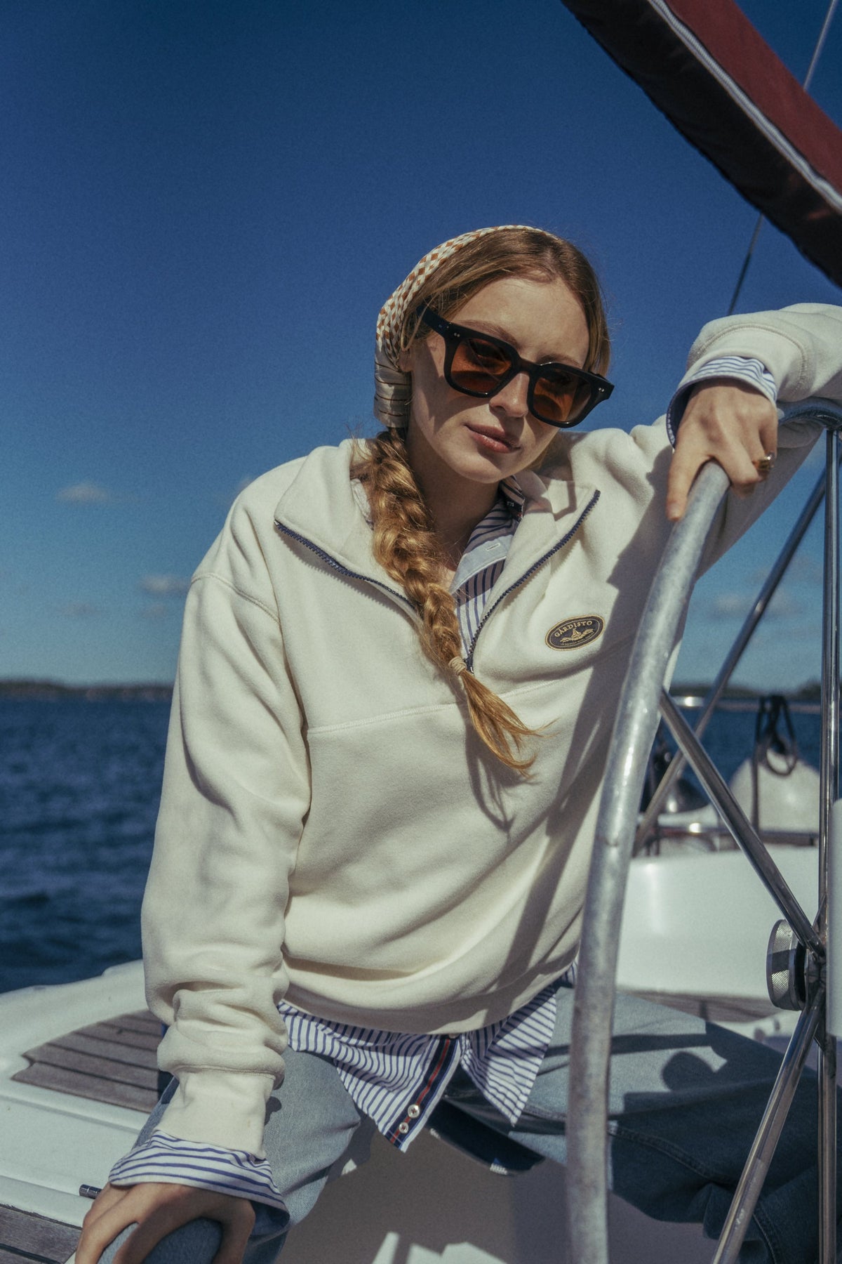 Woman at the helm of a sailing boat wearing the Gårdisto Fleece Half-Zip in sand.