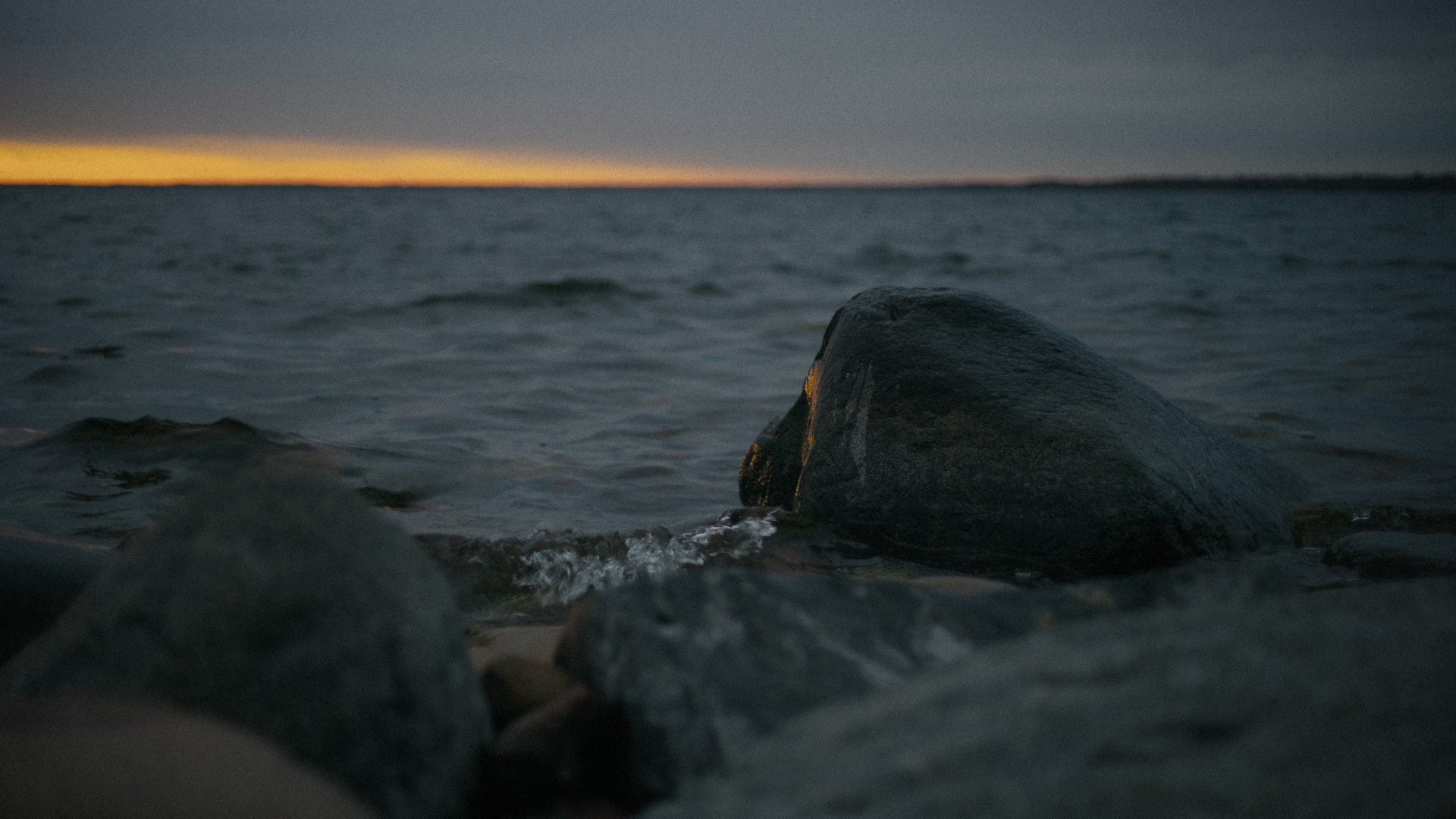Klippestrand og åpent hav under en gyllen horisont.